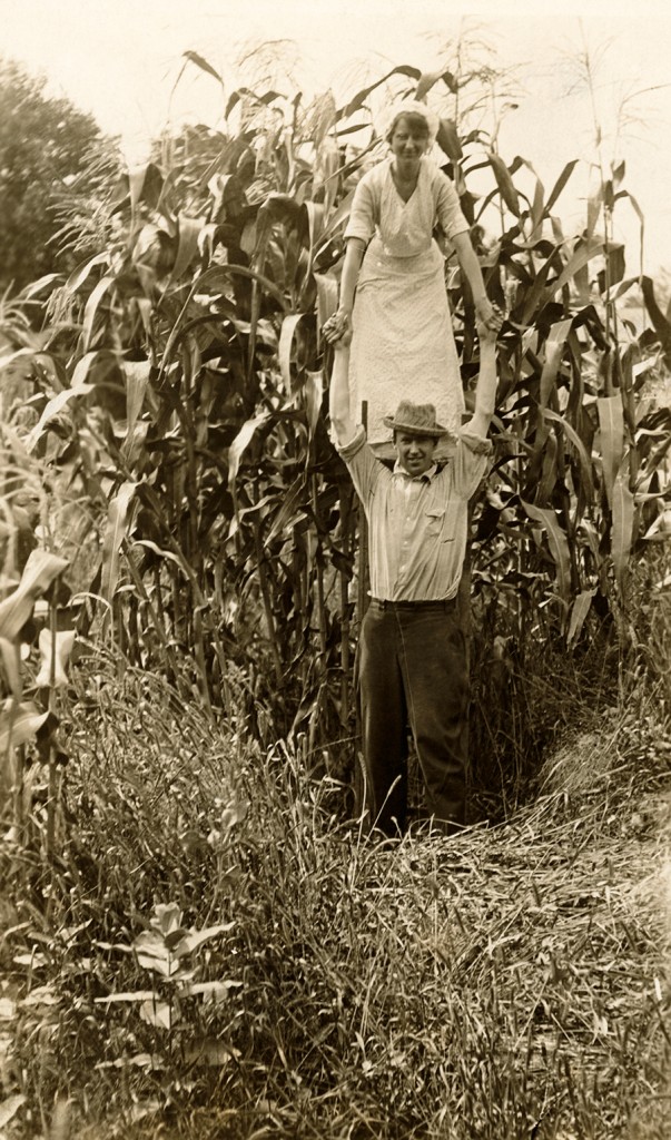 A woman on a farmer’s shoulder emphasizes a corn crop’s height in Minnesota, 1916